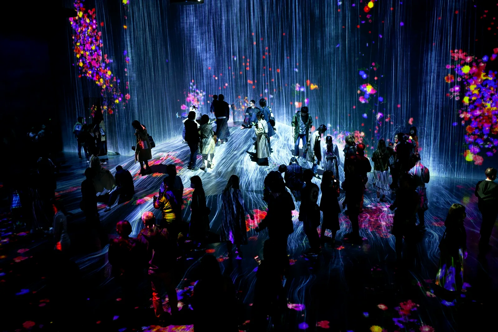 Visitors exploring cascading light and flower projections at an immersive digital installation